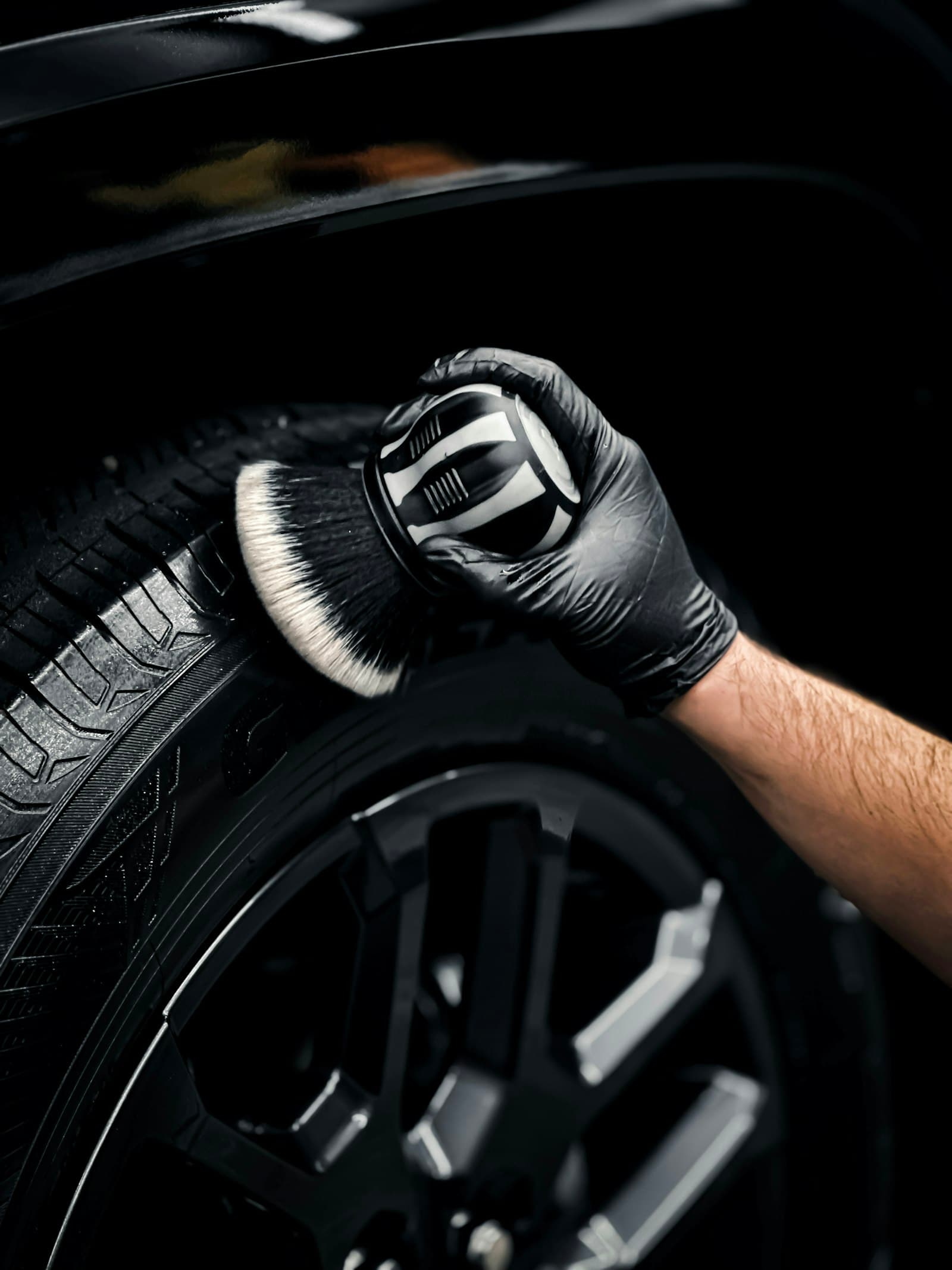 Detailer in black gloves cleaning a tire with a brush during a mobile detail